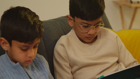 Two-Young-Boys-Sitting-On-Sofa-At-Home-Playing-Games-Or-Streaming-Onto-Digital-Tablets-2